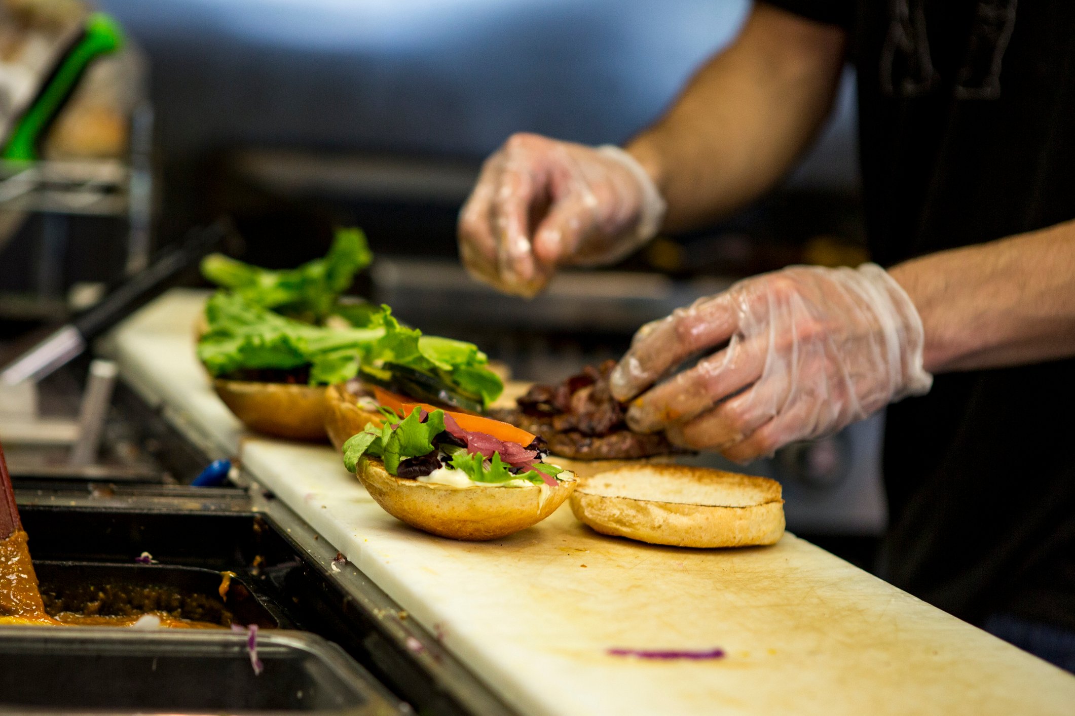 A chef adding toppings to the freshly cooked hamburgers his is preparing.