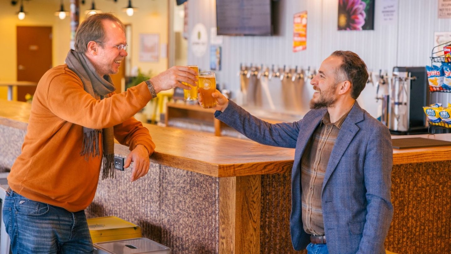 Two men tapping their wine glasses together at a bar