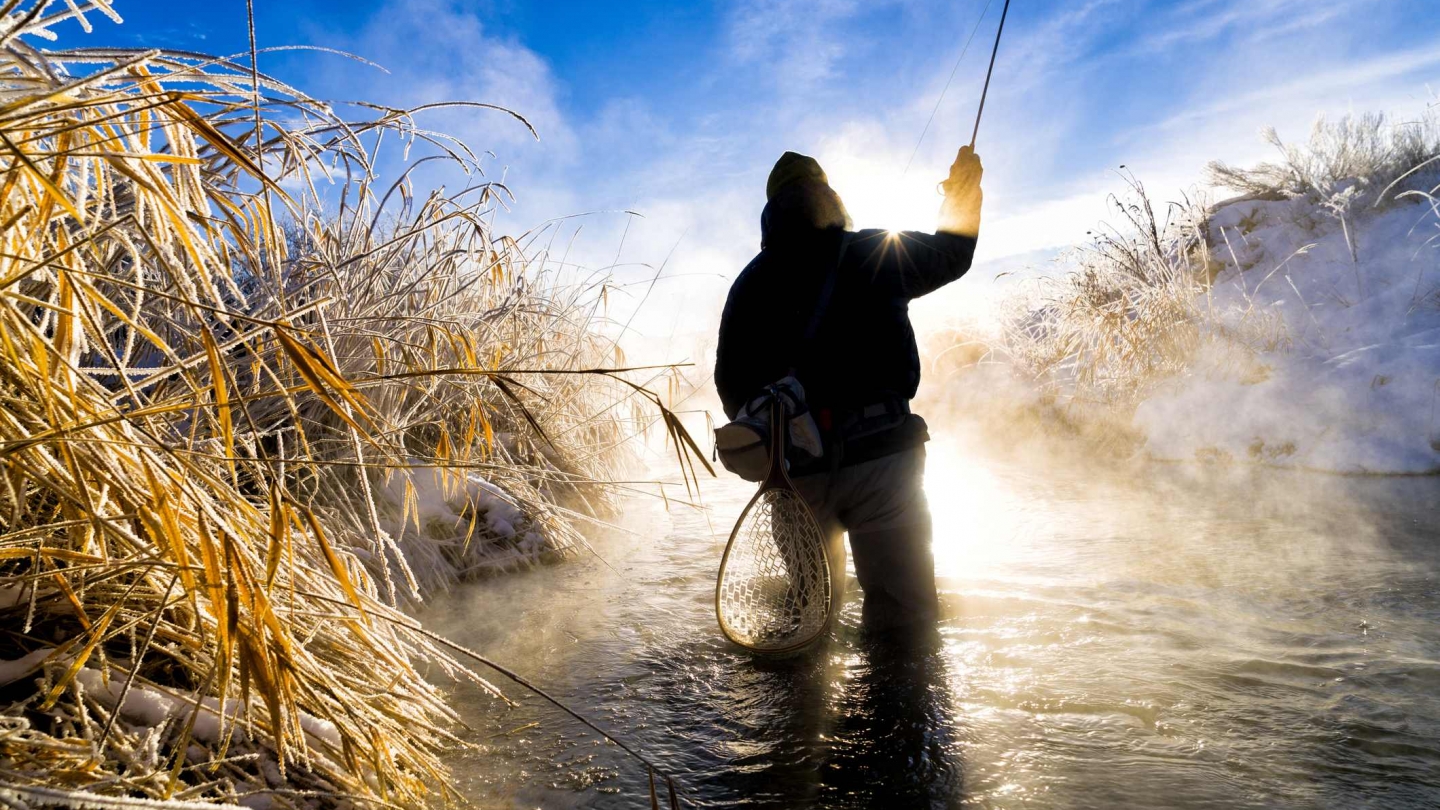 a person fly fishing in a small river at dawn