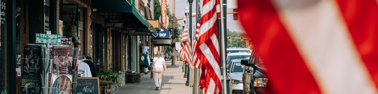 A woman walking down the sidewalk lined with American flags and shops.