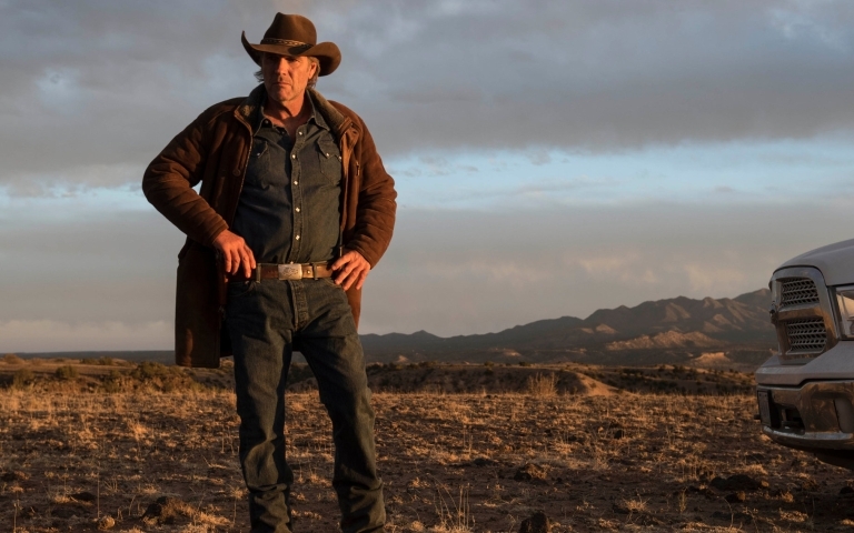 Kevin Costner standing with the mountains behind him.