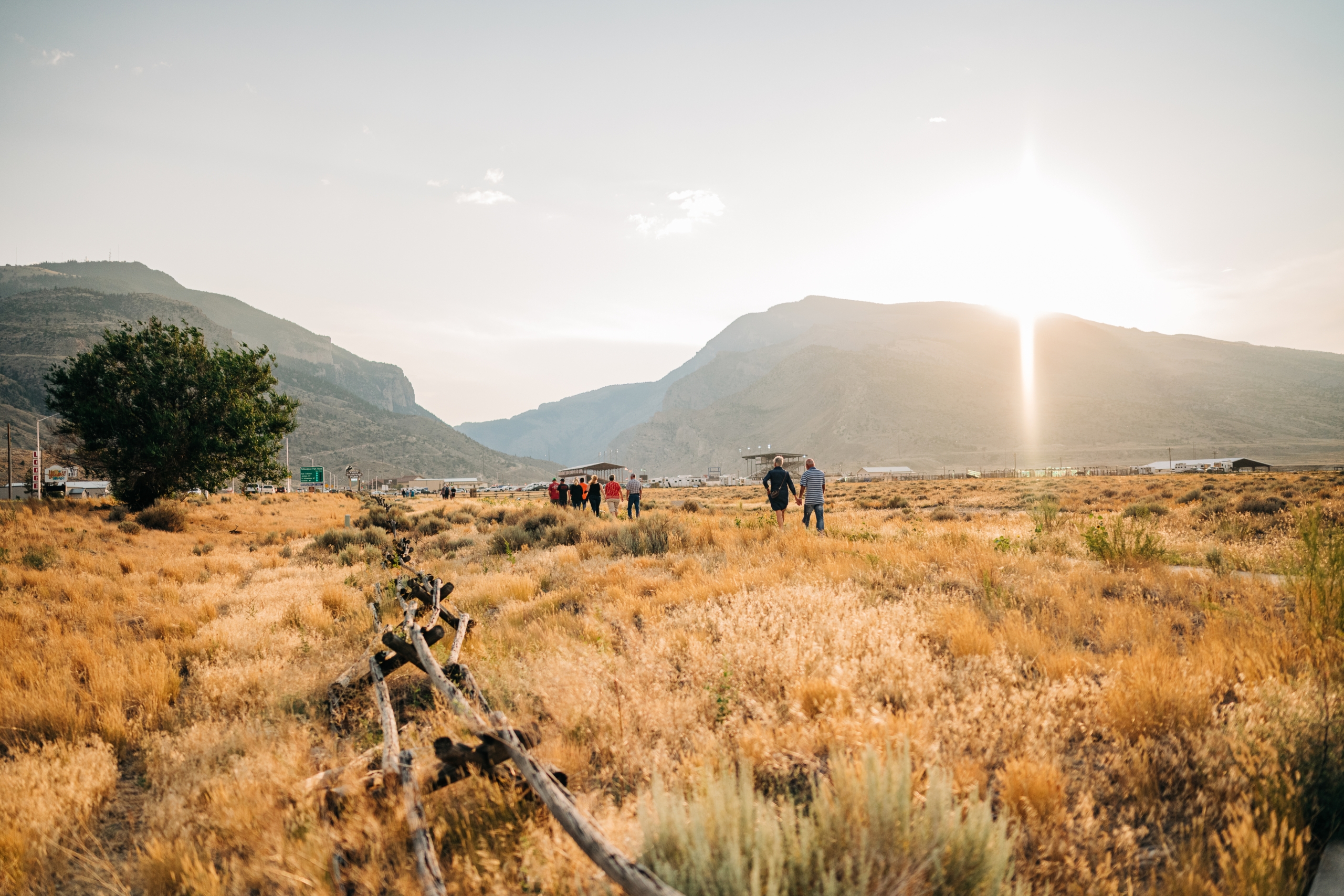 a group of people walking on a trail with the mountains in the foreground and the sun peaking over the mountain