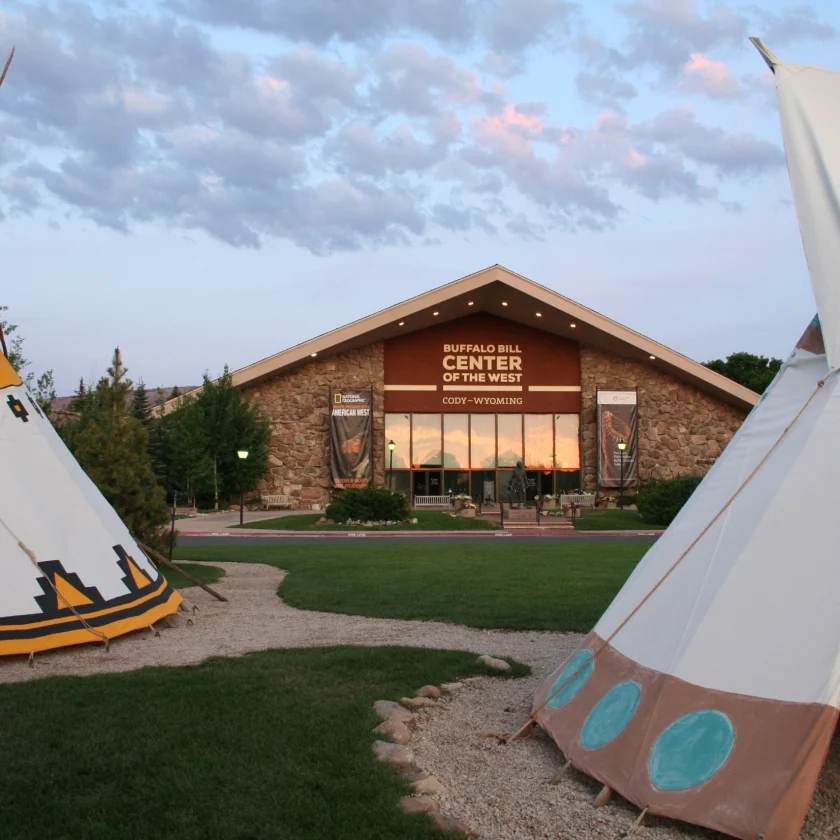 Two colorful teepees stand in front of a modern building, creating a unique blend of nature and architecture