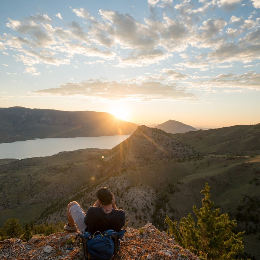 A guy sits on a rock, enjoying the view of a tranquil lake and stunning mountain scenery.