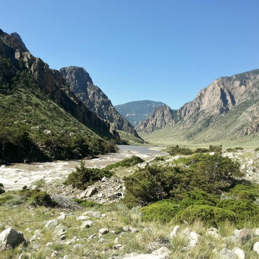 A picturesque river meanders through a green valley, bordered by stunning mountain peaks.