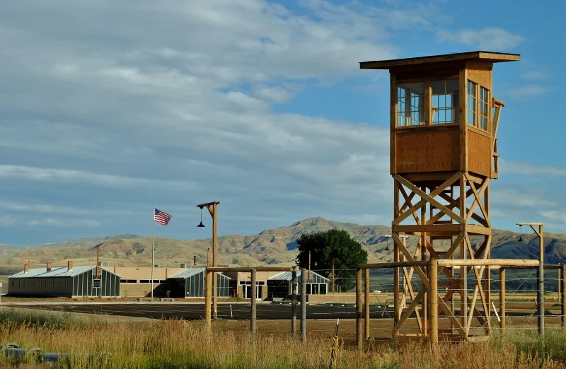 A solitary guard tower stands tall in the center of a vast, open field under a clear blue sky.