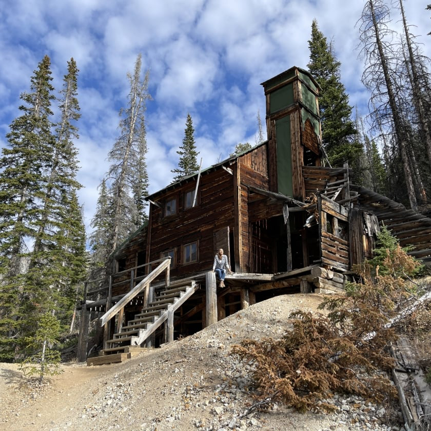 A person stands at the cabin steps in the woods, taking in the tranquil atmosphere and beautiful natural scenery.