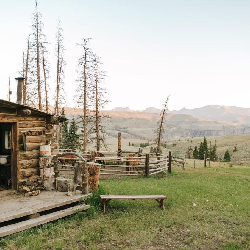 A rustic cabin surrounded by mountains, complete with a bench to enjoy the beautiful mountain scenery.