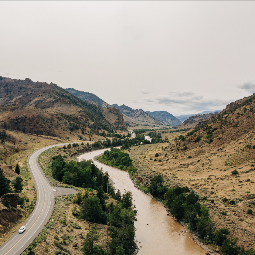 A winding road snakes through towering mountains, with a river flowing gracefully beside it, creating a picturesque view.