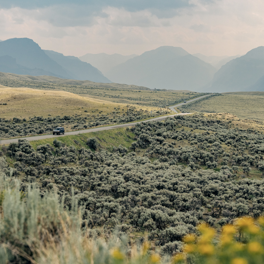 A car on a picturesque mountain road, framed by majestic peaks and vibrant nature all around