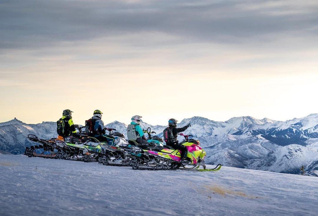 A group of friends in the mountains on colorful snowmobiles