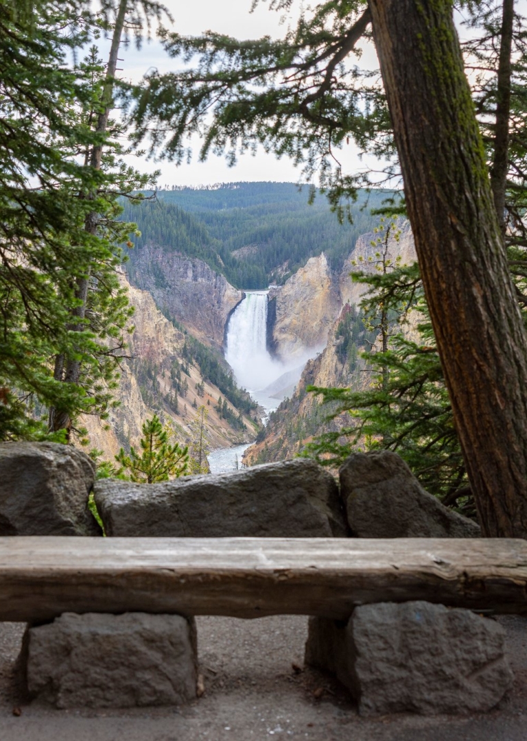 A wooden bench lookout where you can view a large waterfall from the mountains