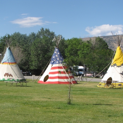 Three teepees set up on the grass of a campground.