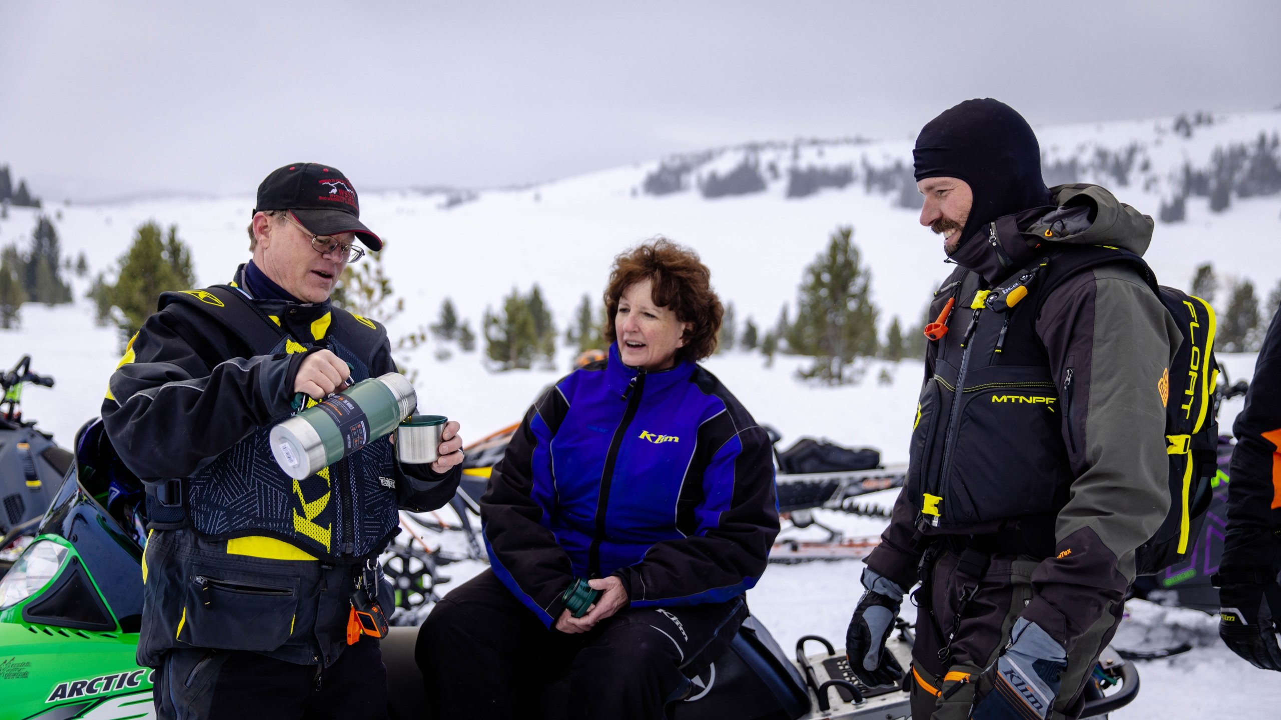 three people taking a break snowmobiling having coffee