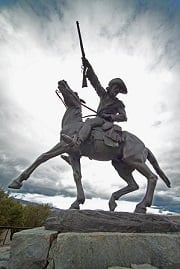 A statue of Buffalo Bill on a horse raising his gun in the air.