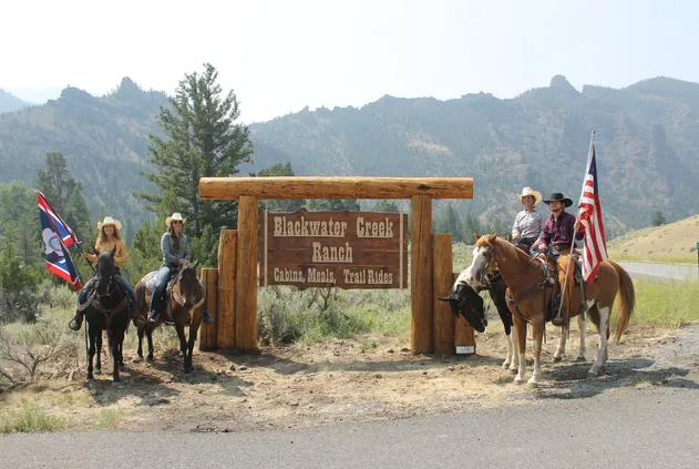 4 people on horses beside the Blackwater Creek Ranch sign