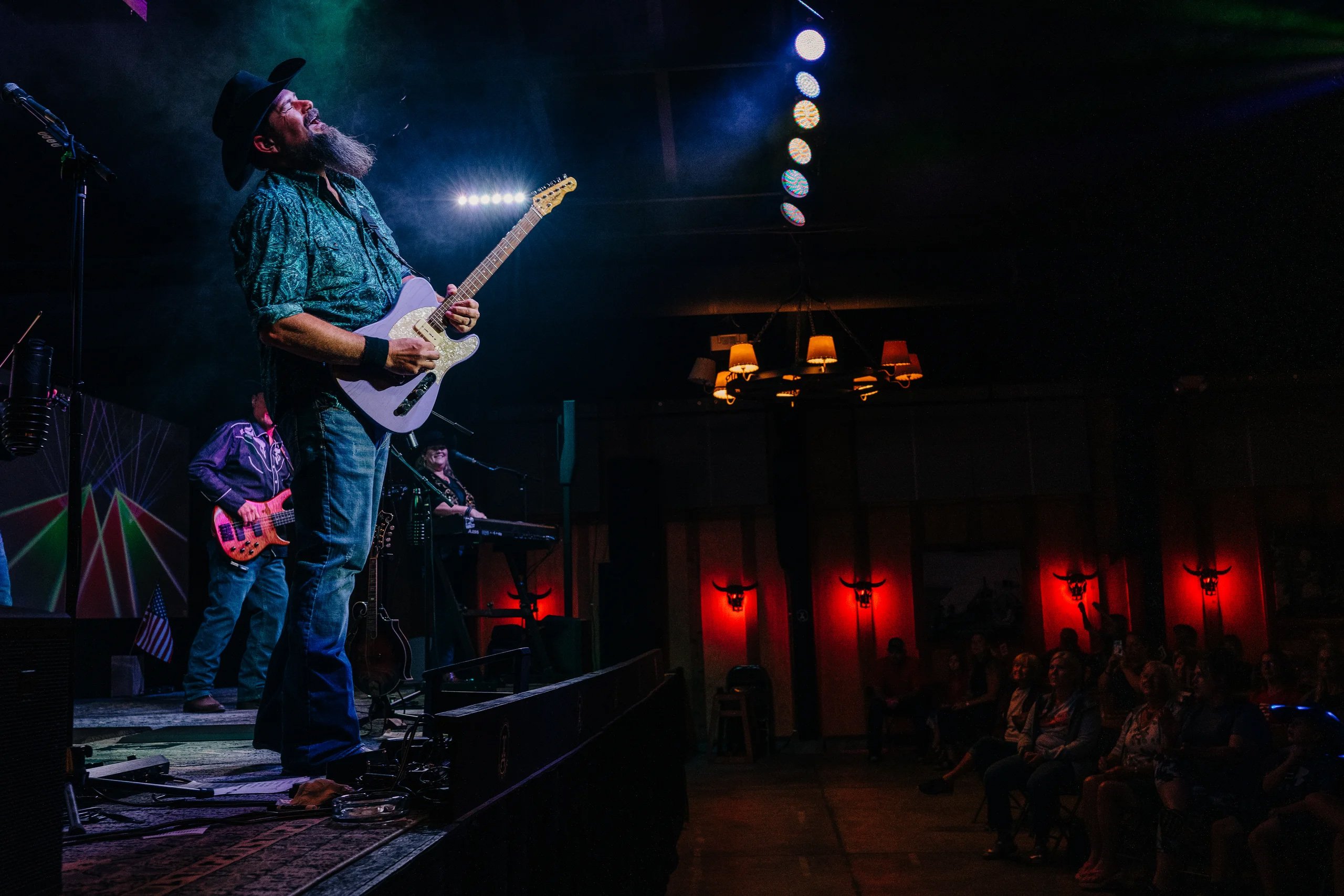 A bearded man strumming a guitar passionately on stage, captivating the audience with his music