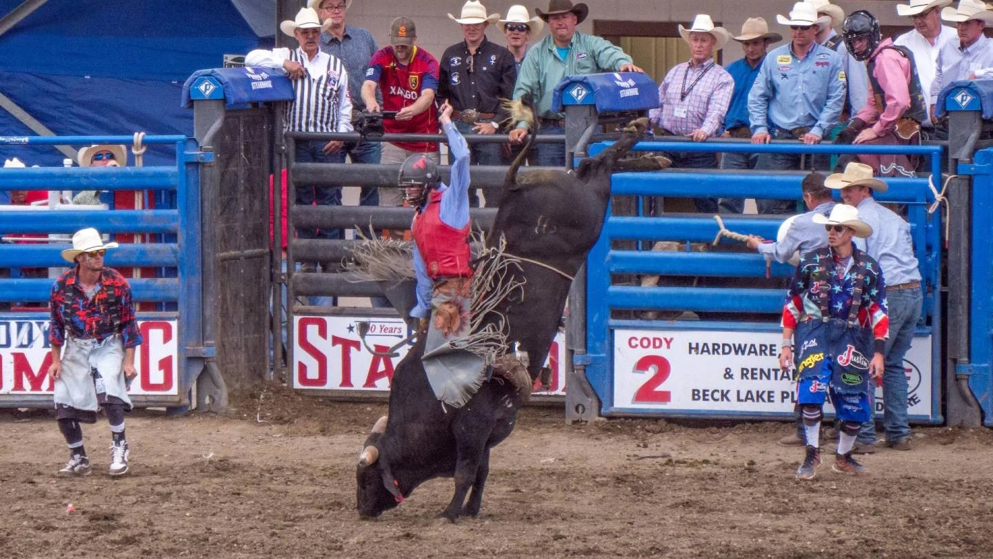 A man bull riding with people with cowboy hats watching at the Cody Stampede-Rodeo