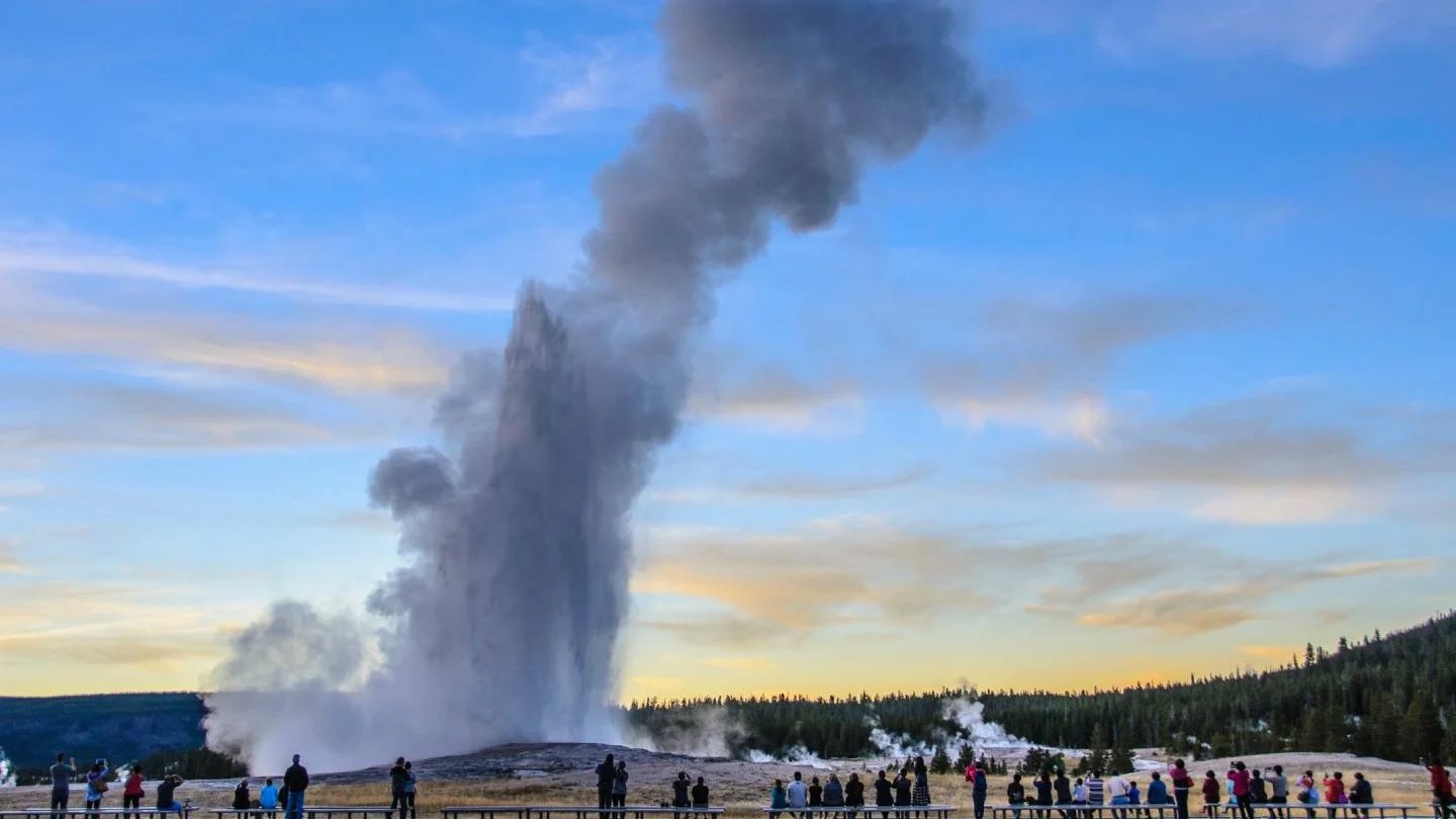 Old fairthful geyser under the clear sky with people watching