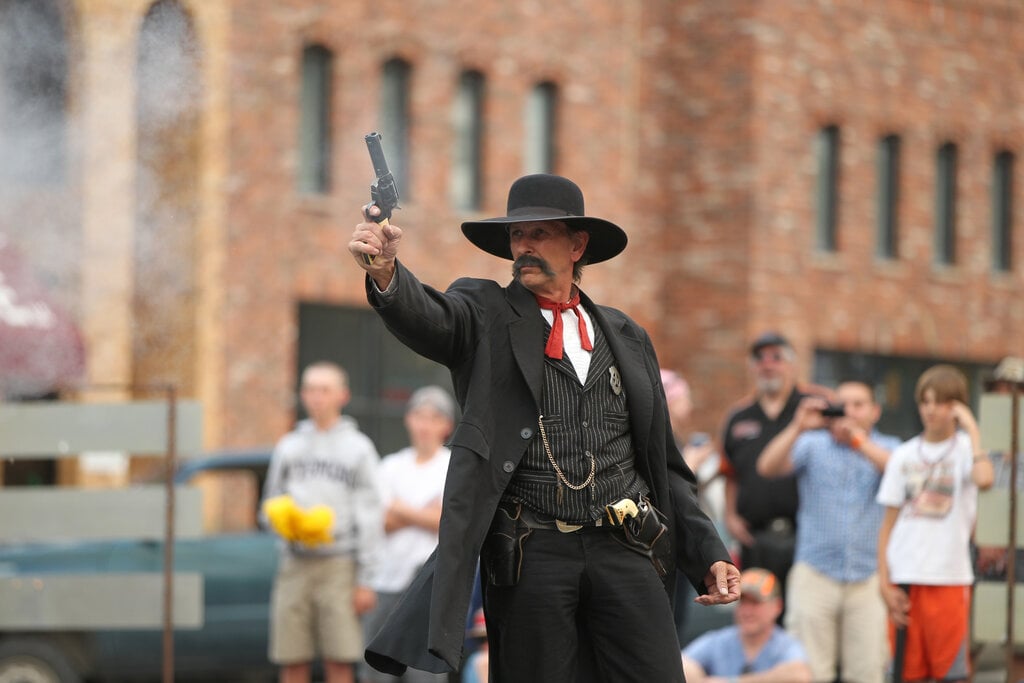 A man in a black suit stands confidently outside the Irma Hotel, showcasing a professional look and gunfights