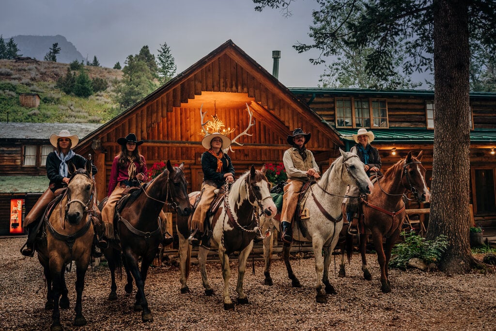 Five individuals on horses gather in front of a rustic lodge, showcasing a perfect blend of nature and camaraderie