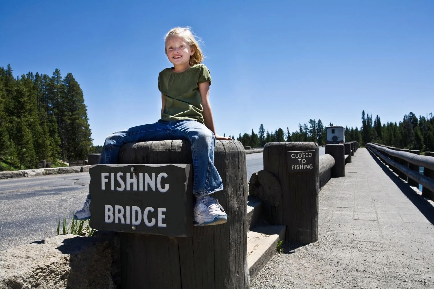 A girl sitting on the wooden fence at the entrance of fishing bridge under clear sky