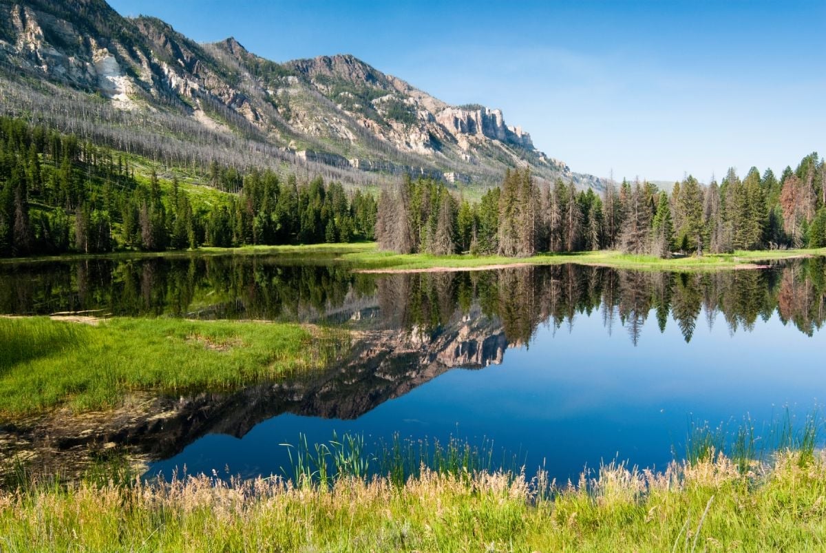 A clear lake reflecting surrounded mountains under blue sky