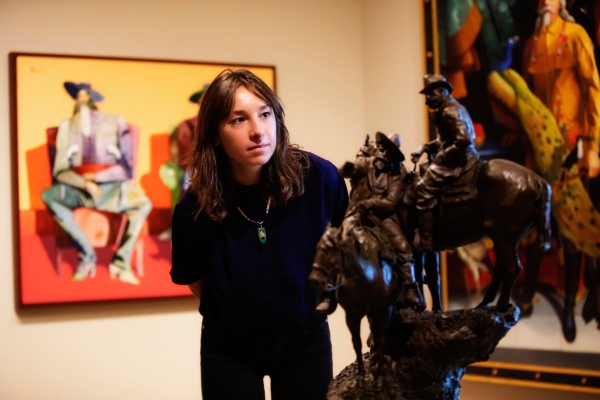 A woman looking at a sculpture of 2 cowboys