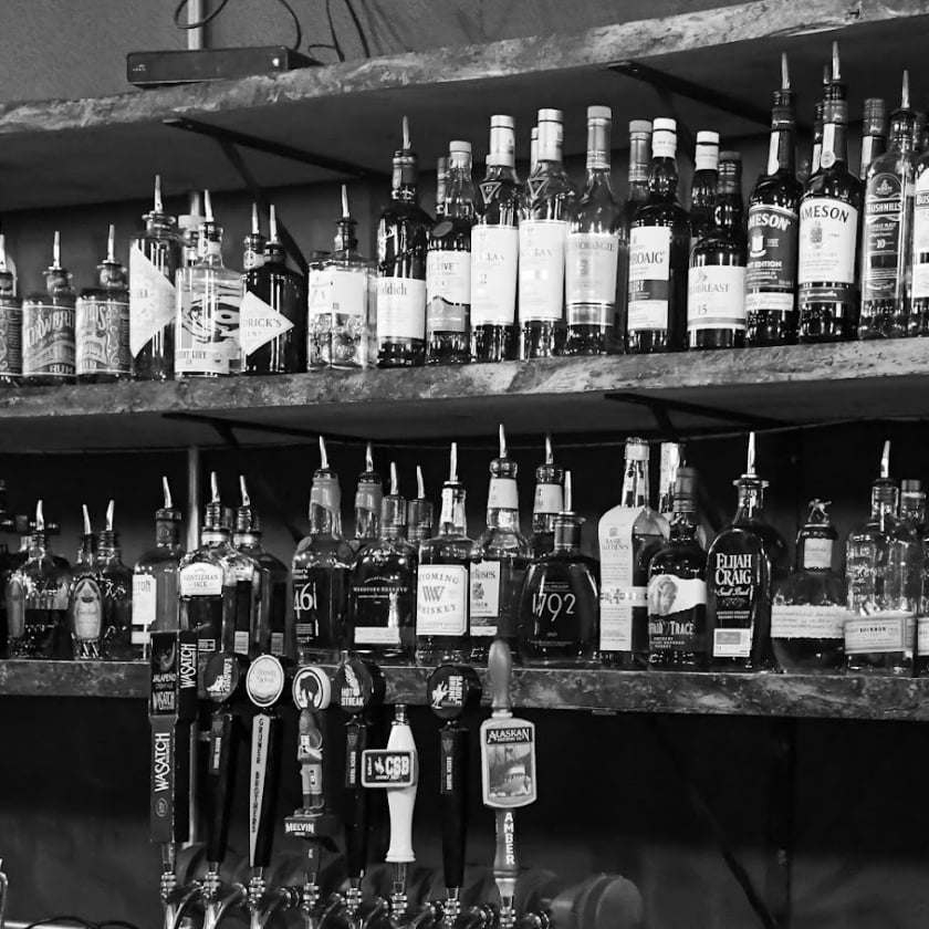 black and white photo of liquor bottles on a shelf inside a bar