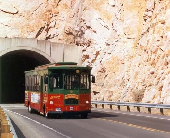 A trolley on the road coming out of a tunnel carved into a mountain.