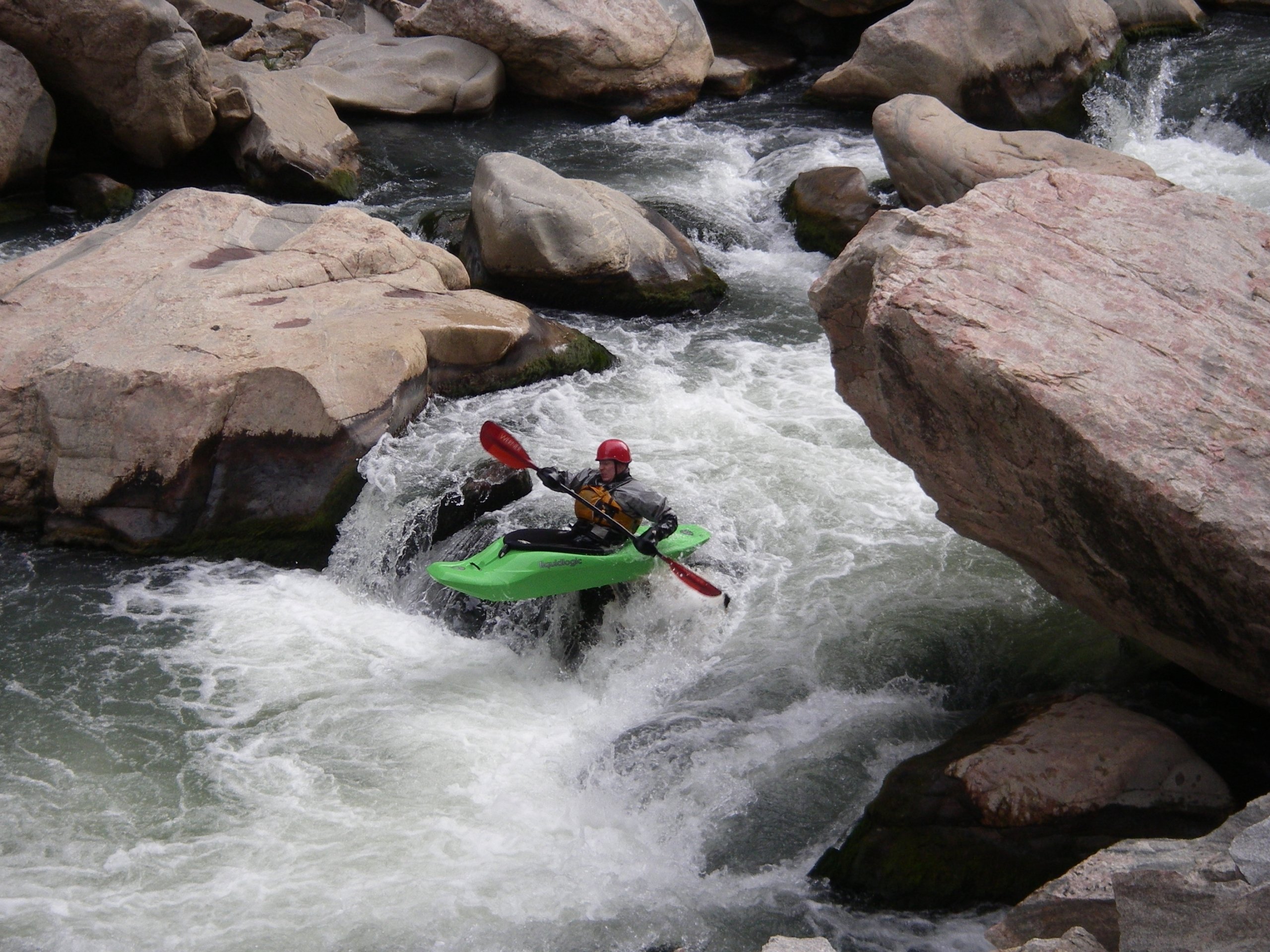 A person kayaking in a green kayak down some rapid in cody