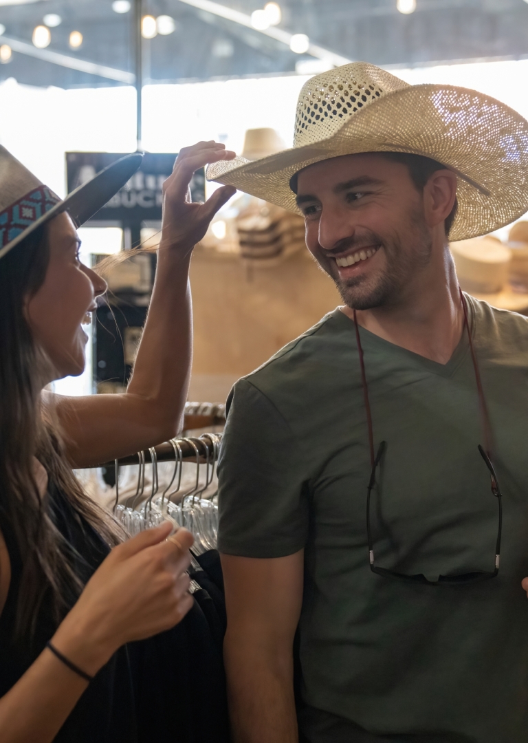 A man and a woman trying on cowboy hats in a shop.