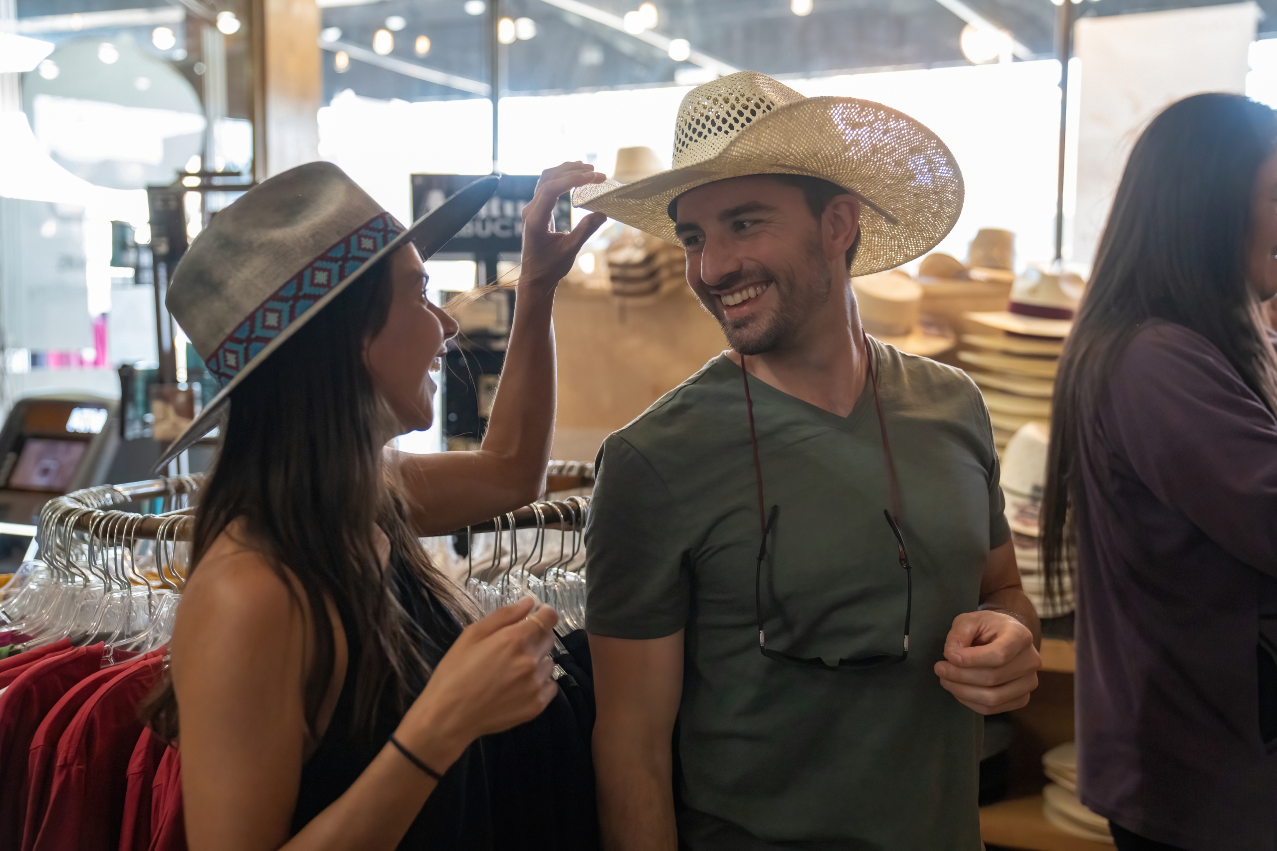 A man and a woman trying on cowboy hats in a shop.