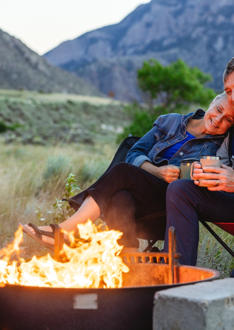 A mature couple sits by a fire near Buffalo Bill Reservoir at dusk