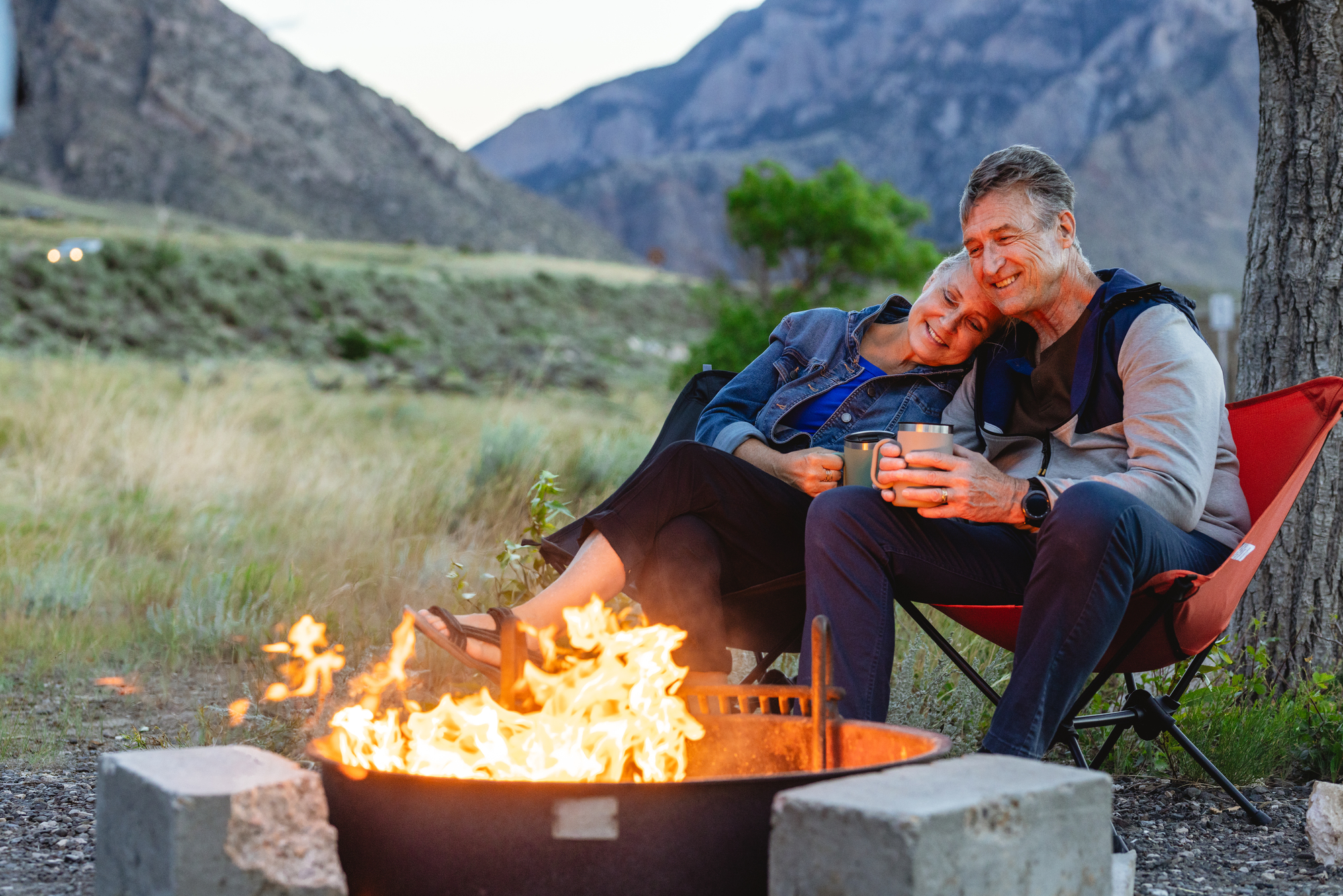 A mature couple sits by a fire near Buffalo Bill Reservoir at dusk